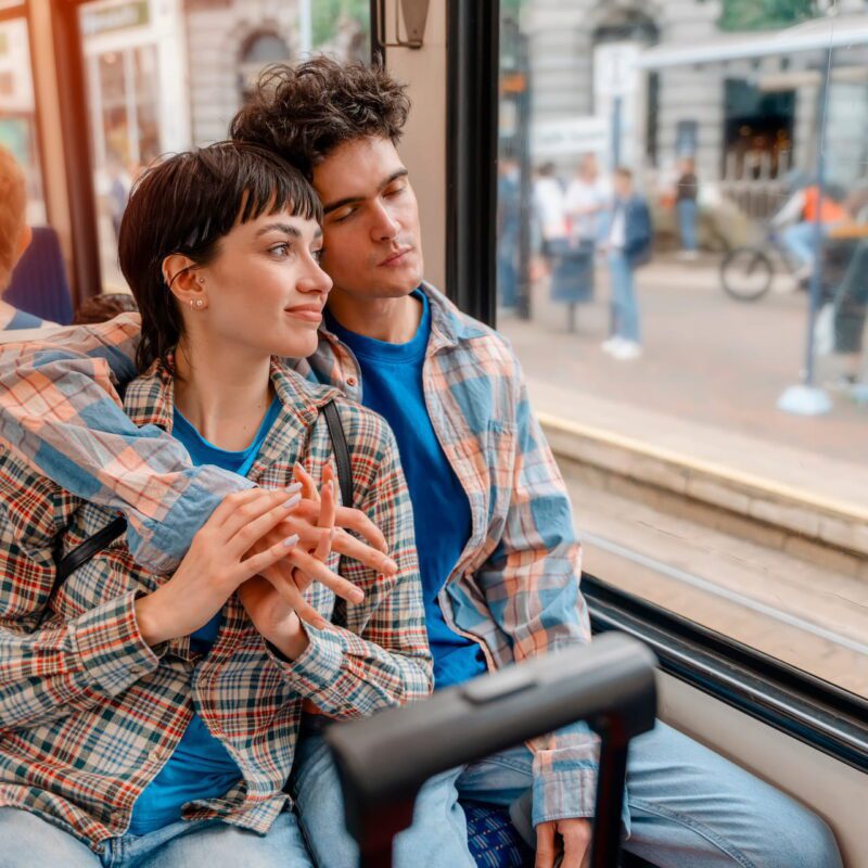 Ein Paar fährt Strassenbahn, man blickt durch die Scheibe auf eine Haltestelle