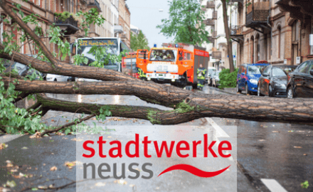 Umgestürzter Baum nach einem Unwetter auf einer Straße, Logo Stadtwerke Neuss